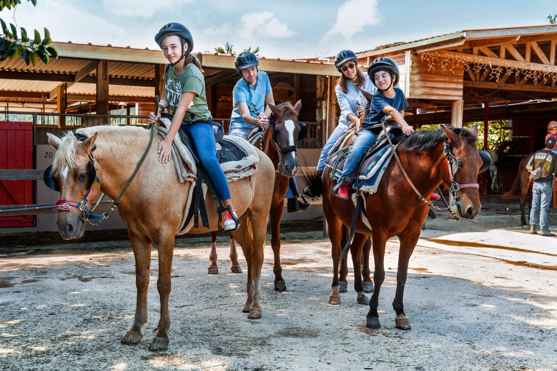 Cuatro personas con casco a caballo en el exterior de un establo.