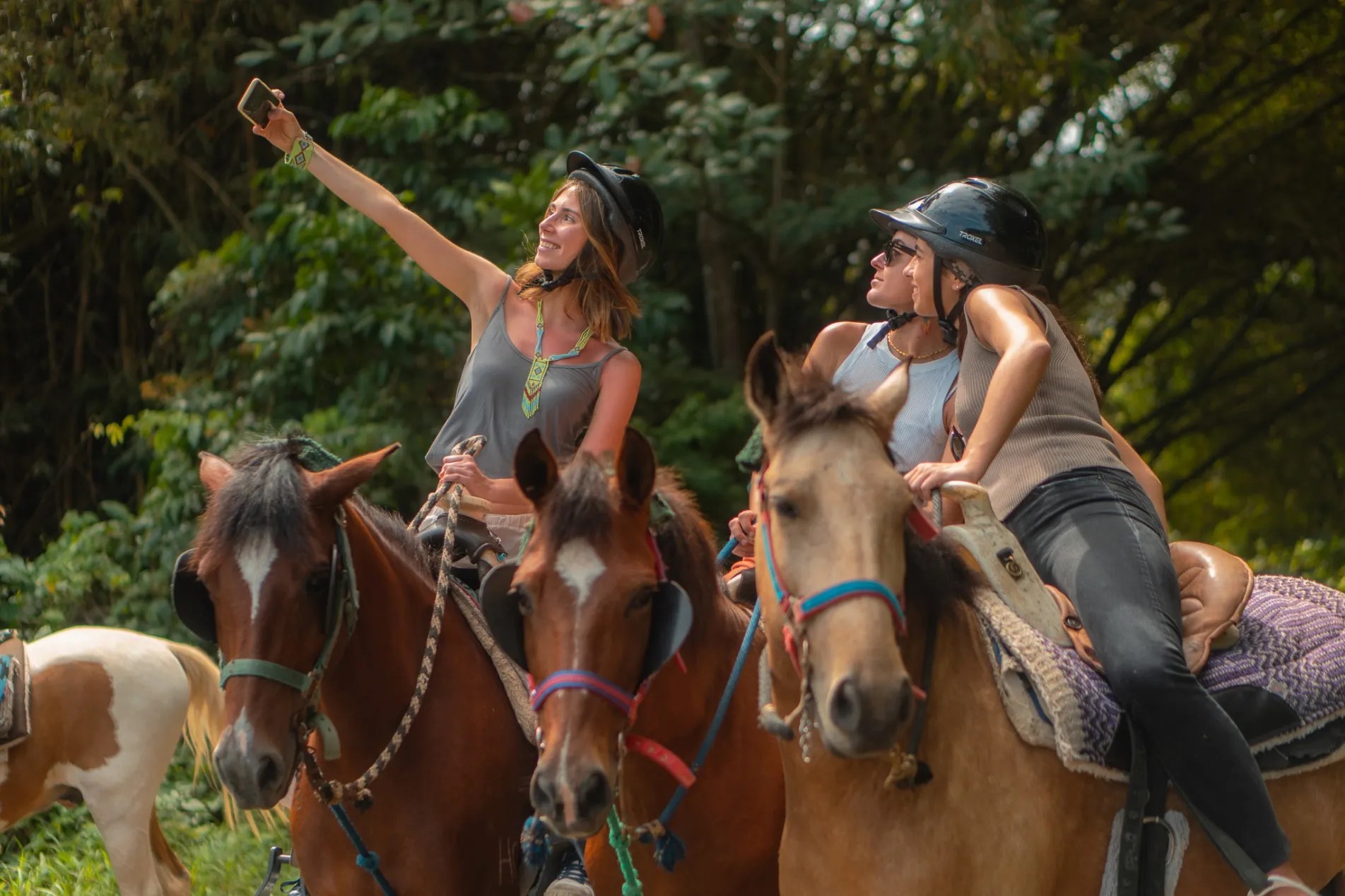 Dos personas a caballo haciéndose un selfie en una zona boscosa.