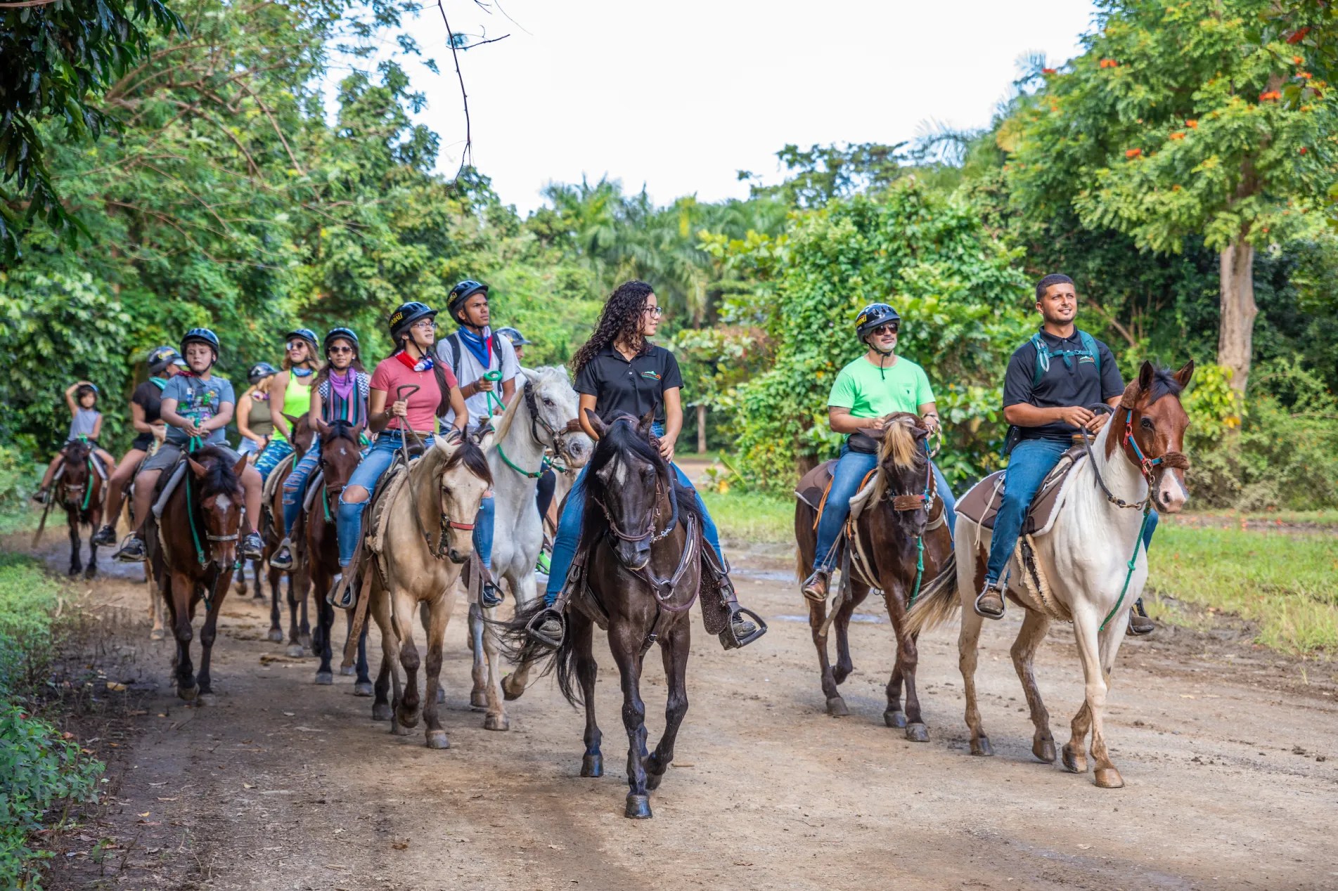 Grupo de personas montando a caballo por un camino de tierra rodeado de exuberante vegetación.