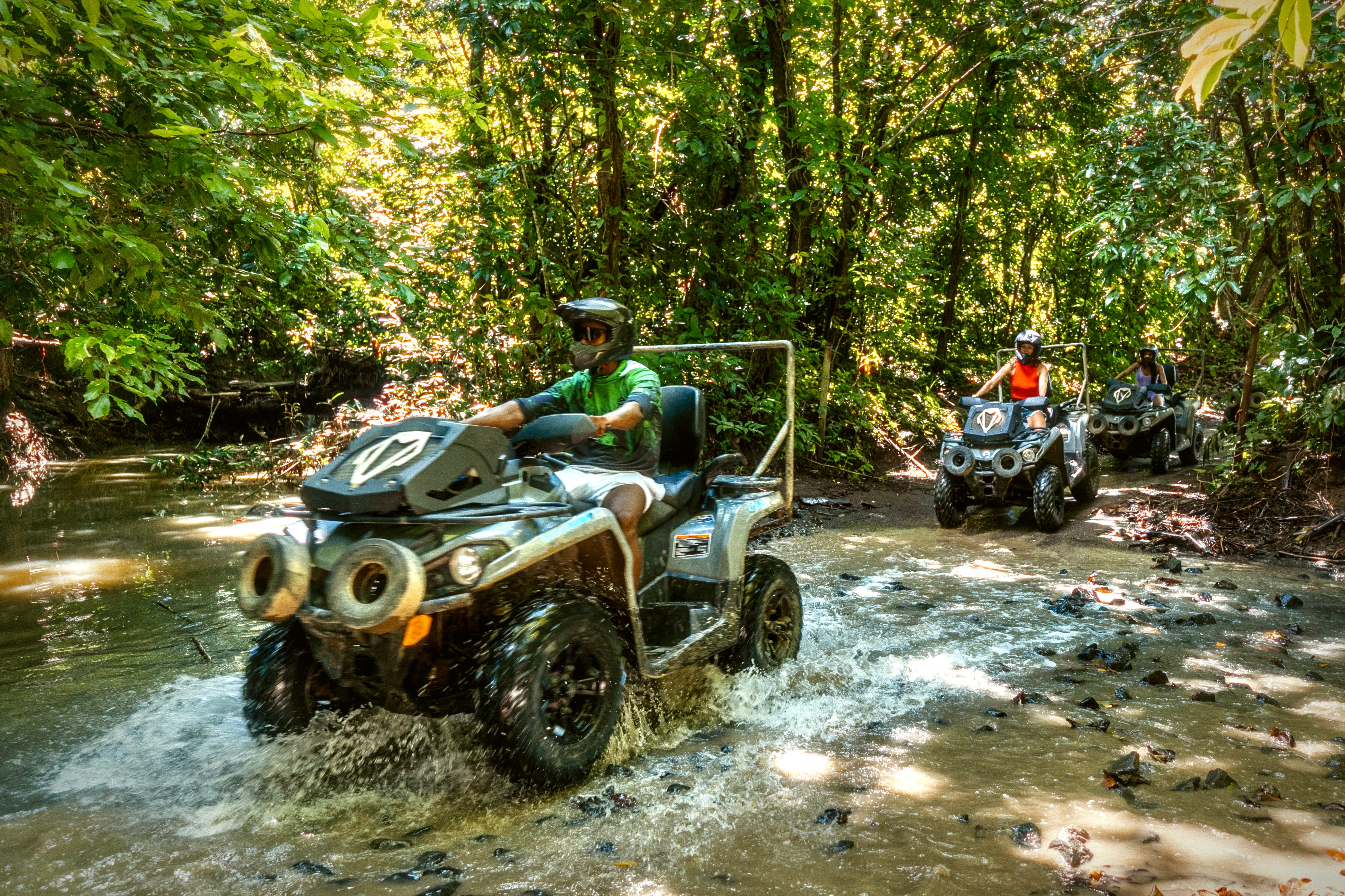 Three people riding ATVs through a forest stream.