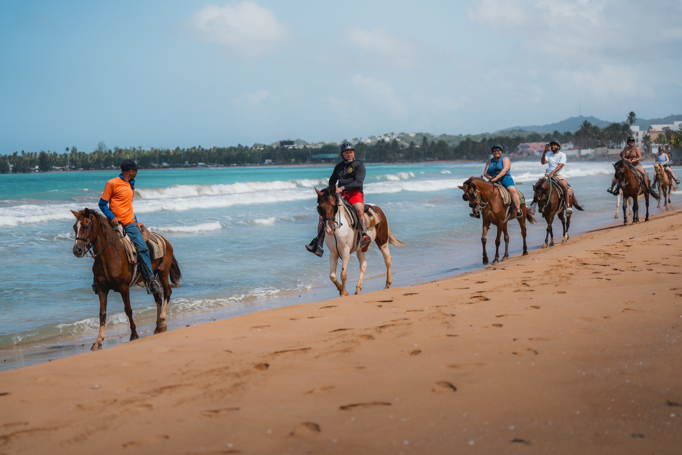 People riding horses along a sandy beach by the ocean.
