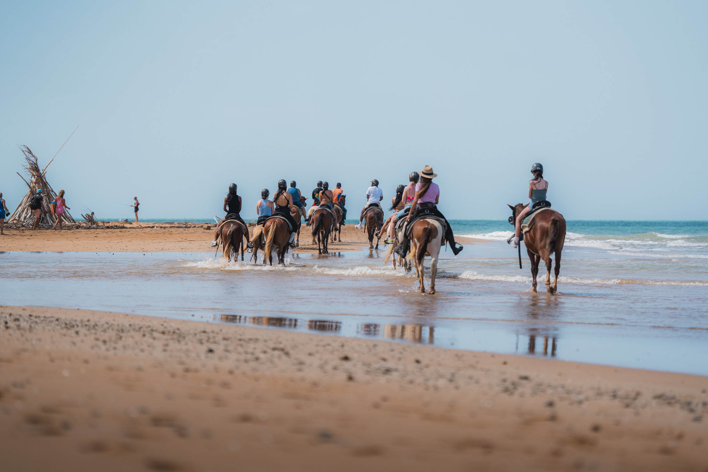 Group of people horseback riding on a beach near the water's edge.
