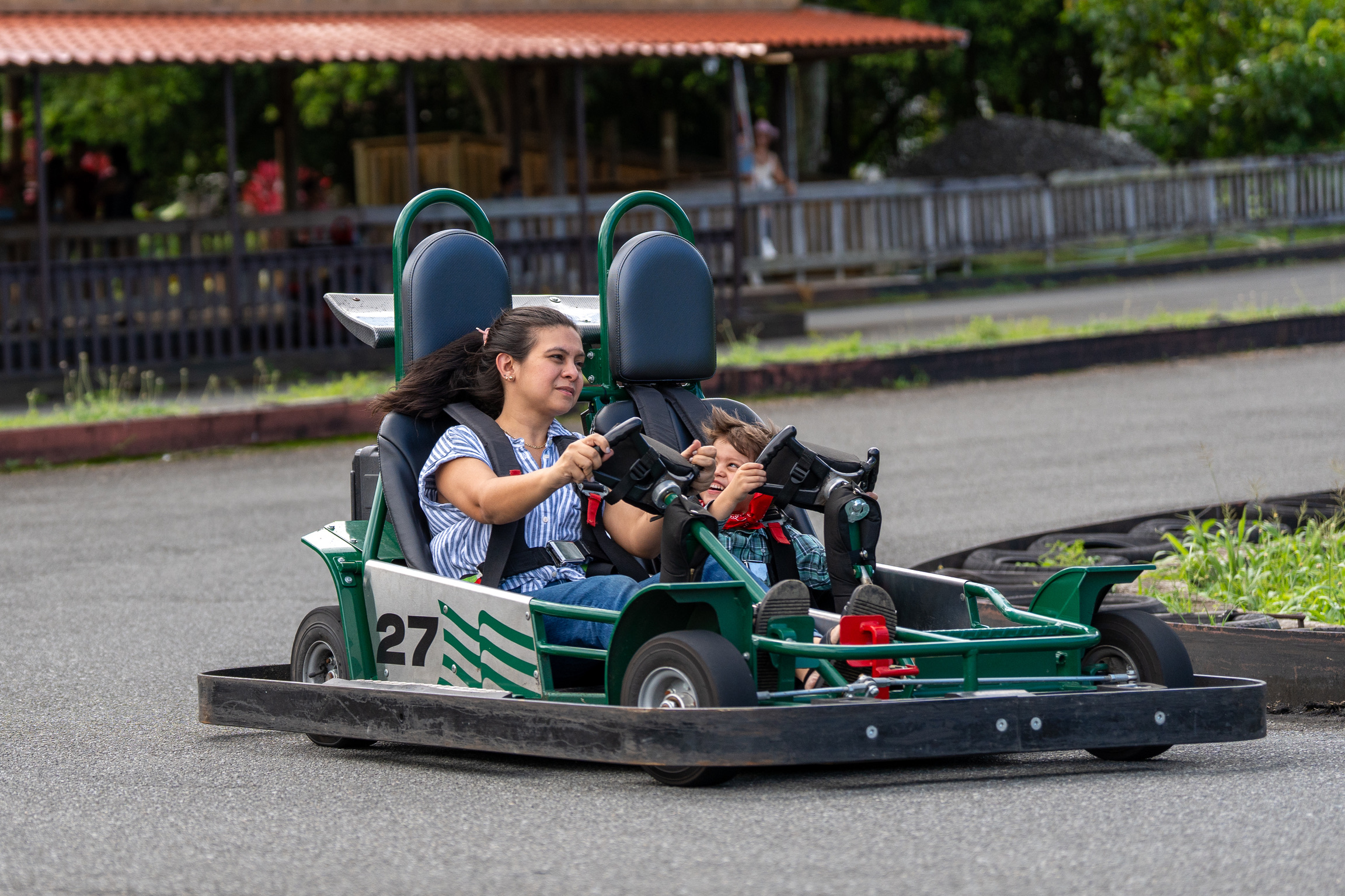 Woman and child driving a green go-kart on an outdoor track.