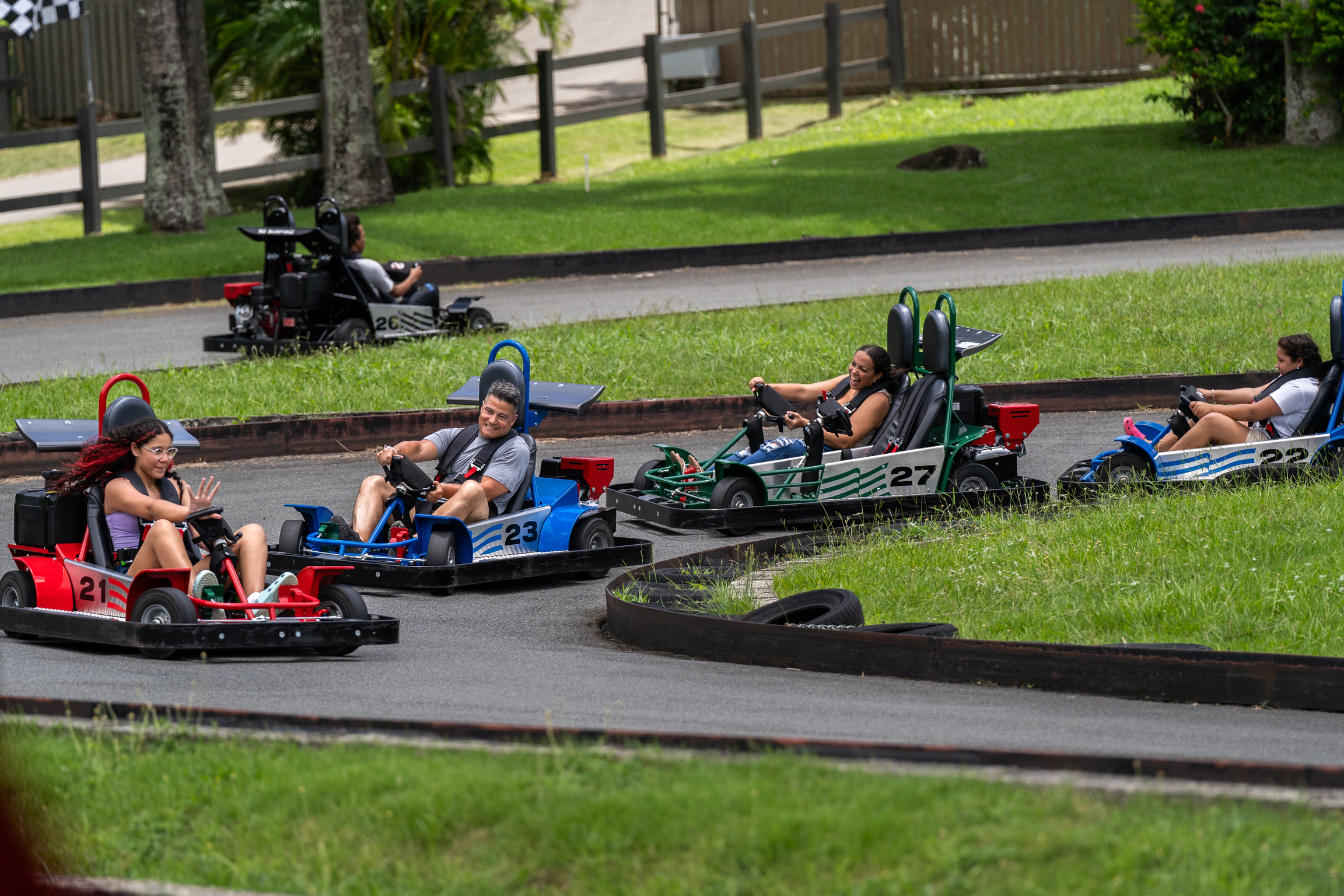 People driving go-karts on a track, surrounded by grass.