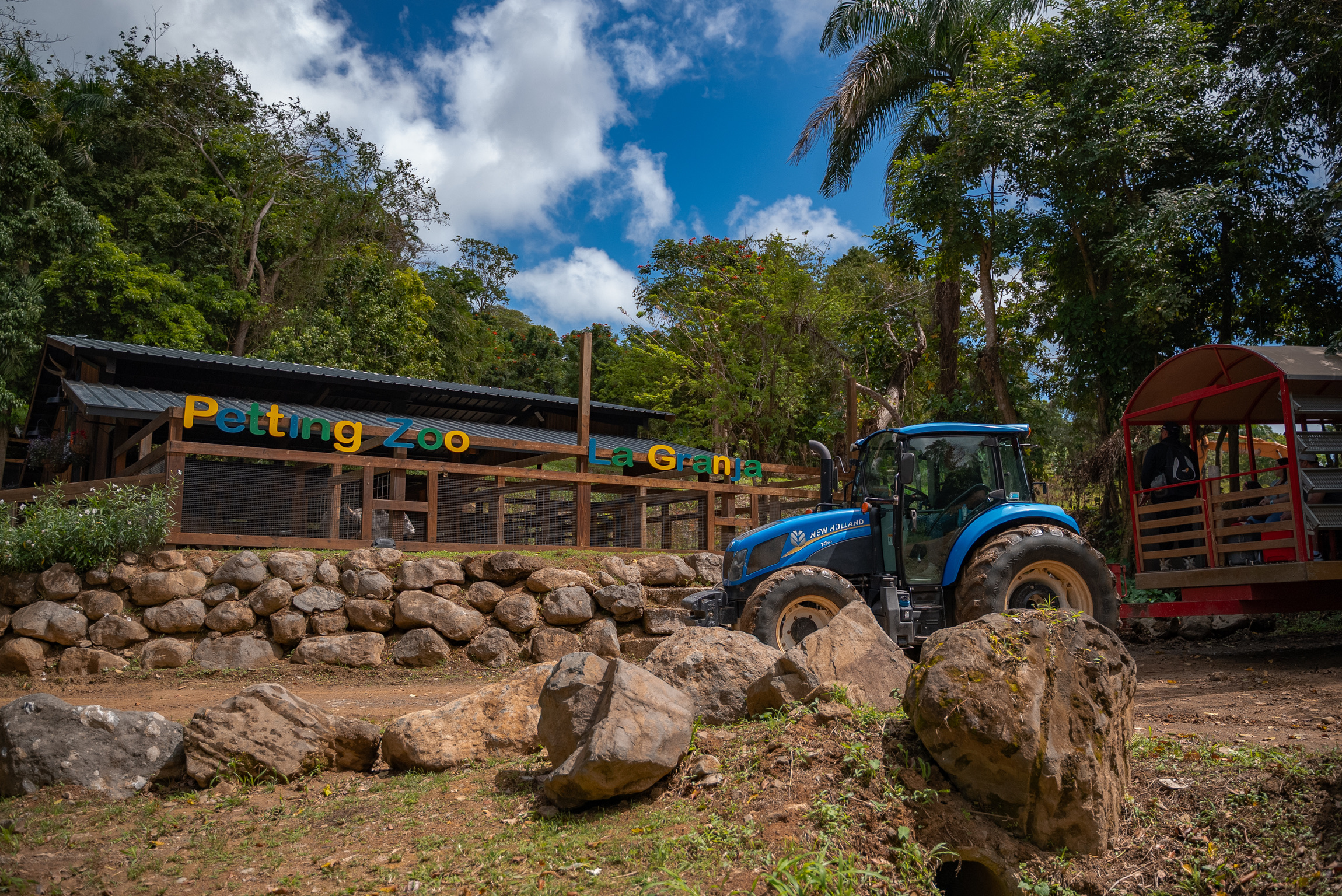Outdoor petting zoo entrance with a blue tractor and wagon under a cloudy sky.