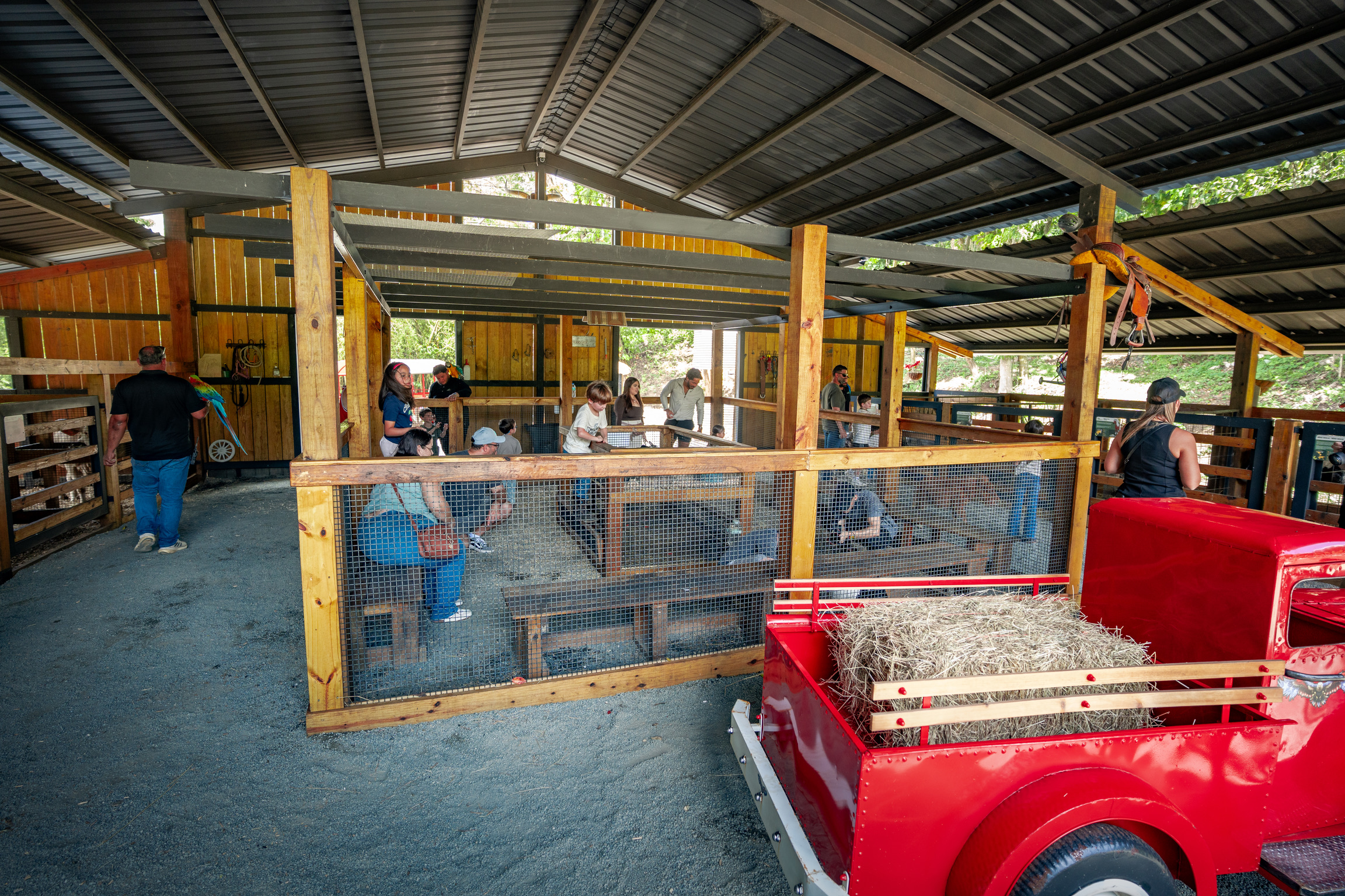 People seated in a rustic barn with a red cart and hay, under a metal roof.