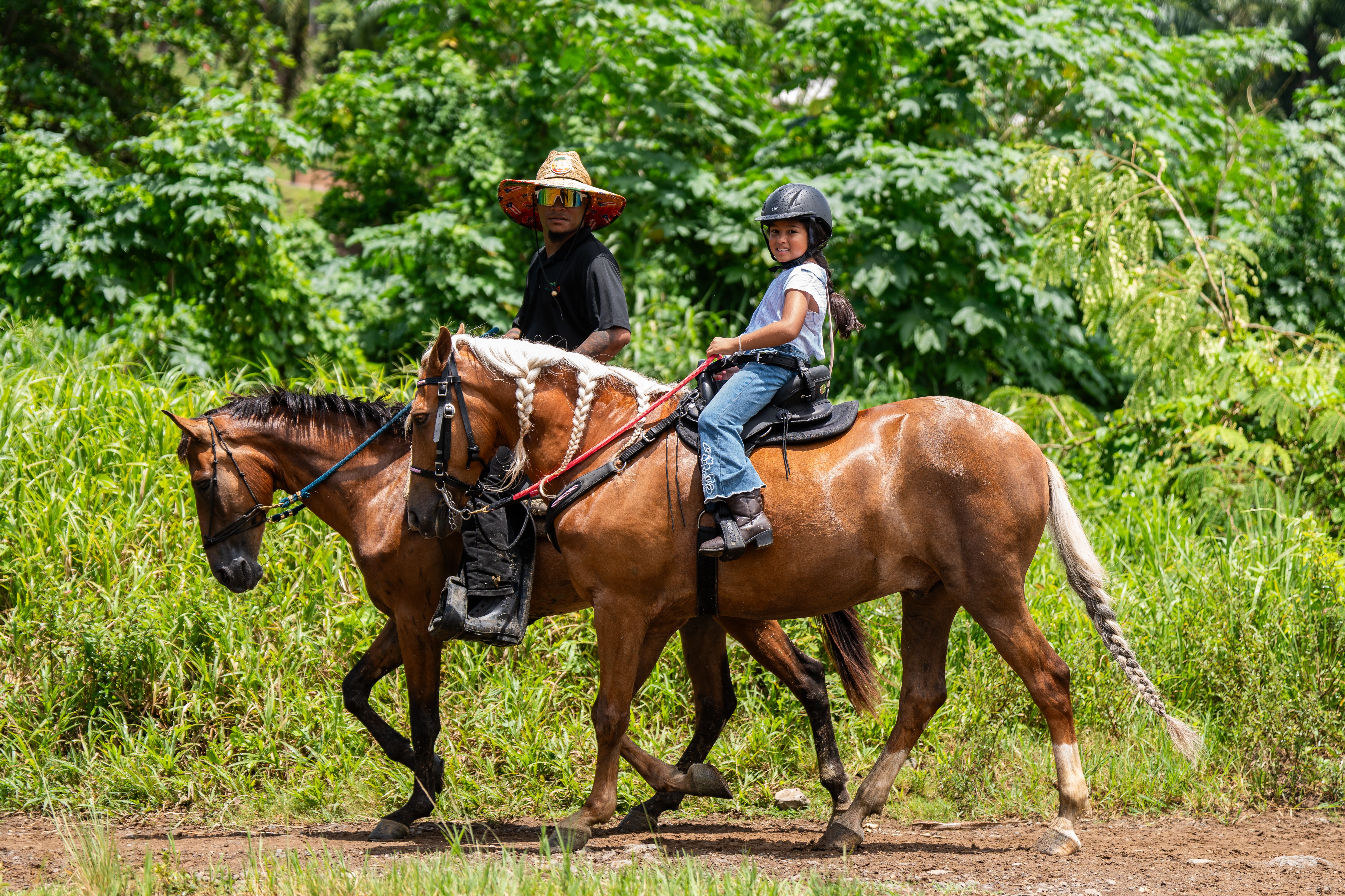 Two people riding horses on a lush green trail.