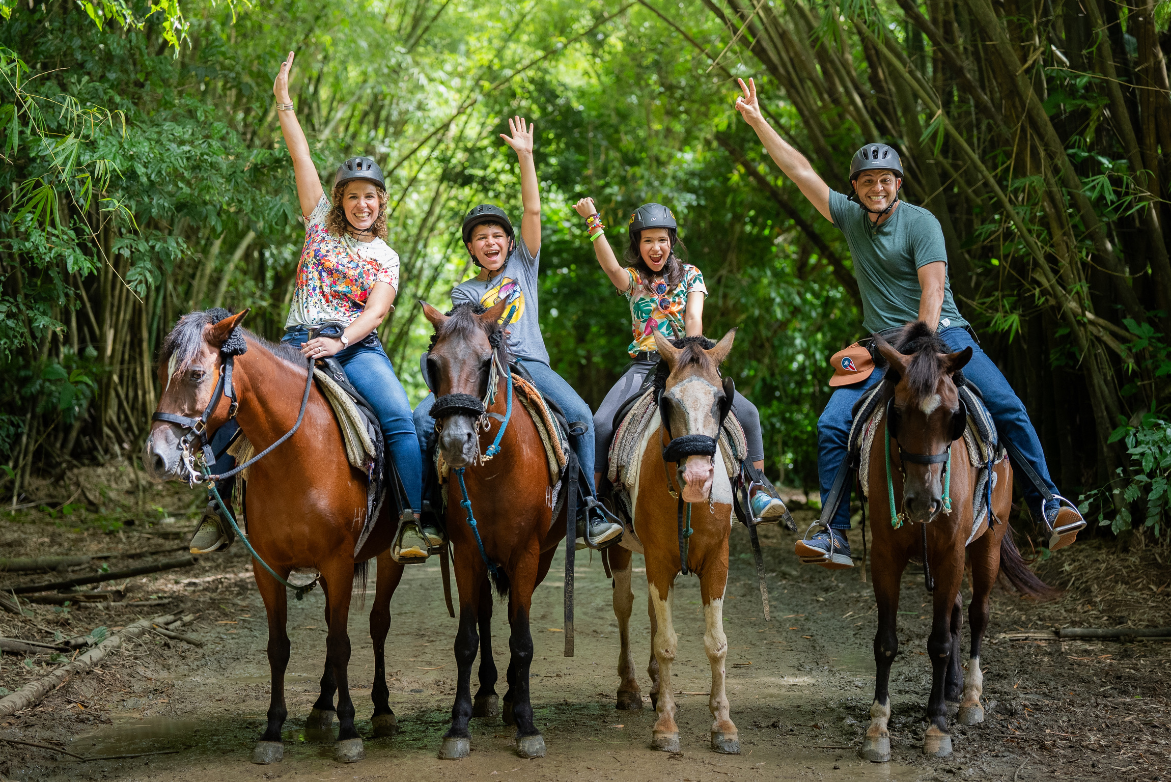 Four people on horses raising hands in a forest.