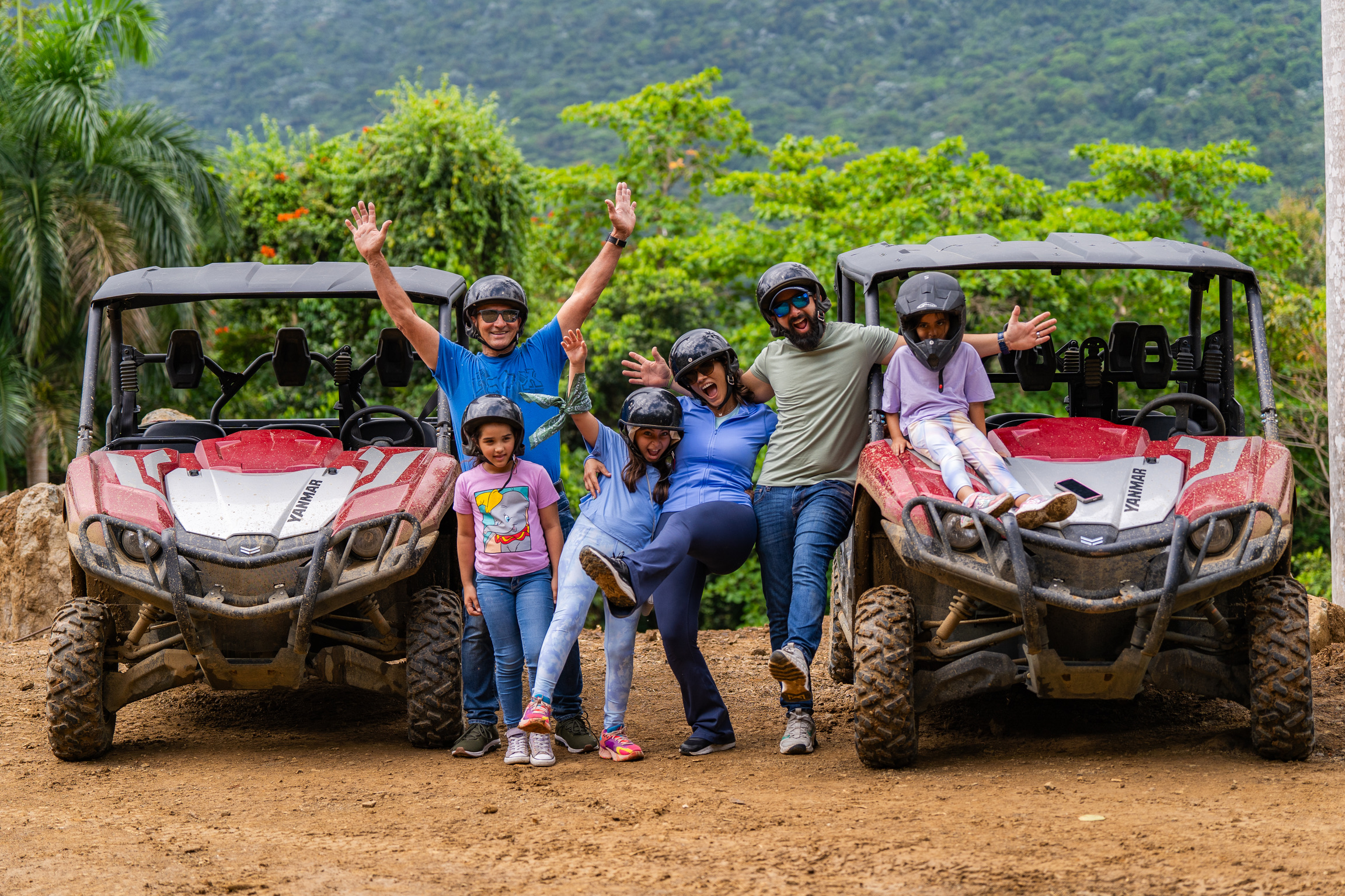 Family posing joyfully between two red ATVs in a lush forest setting.