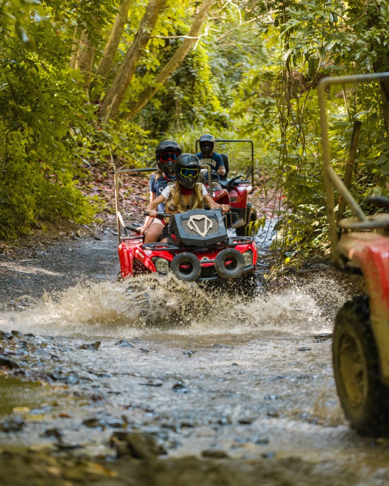 People driving ATVs through a muddy forest trail.