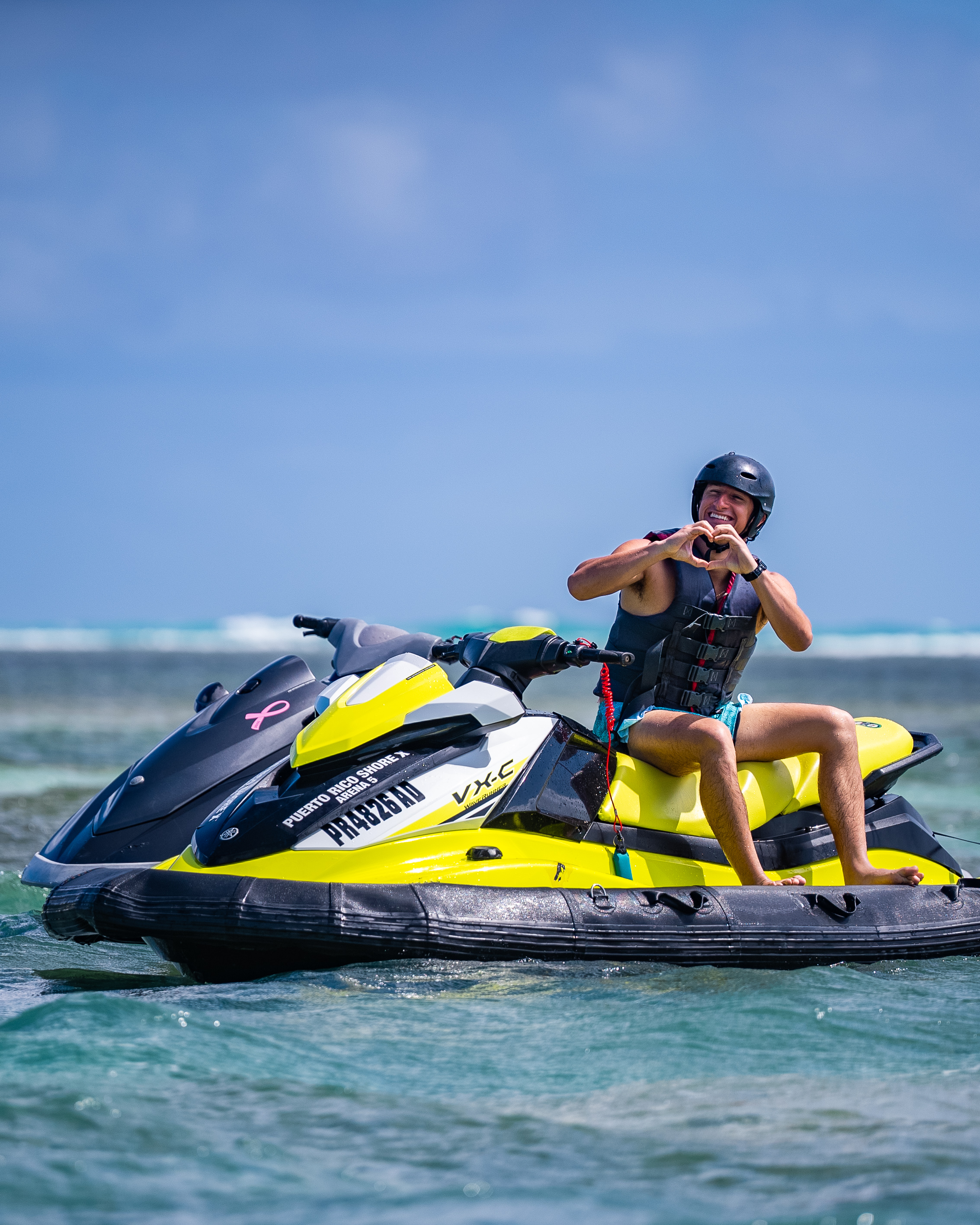 Person on yellow jet ski making heart shape with hands on ocean.