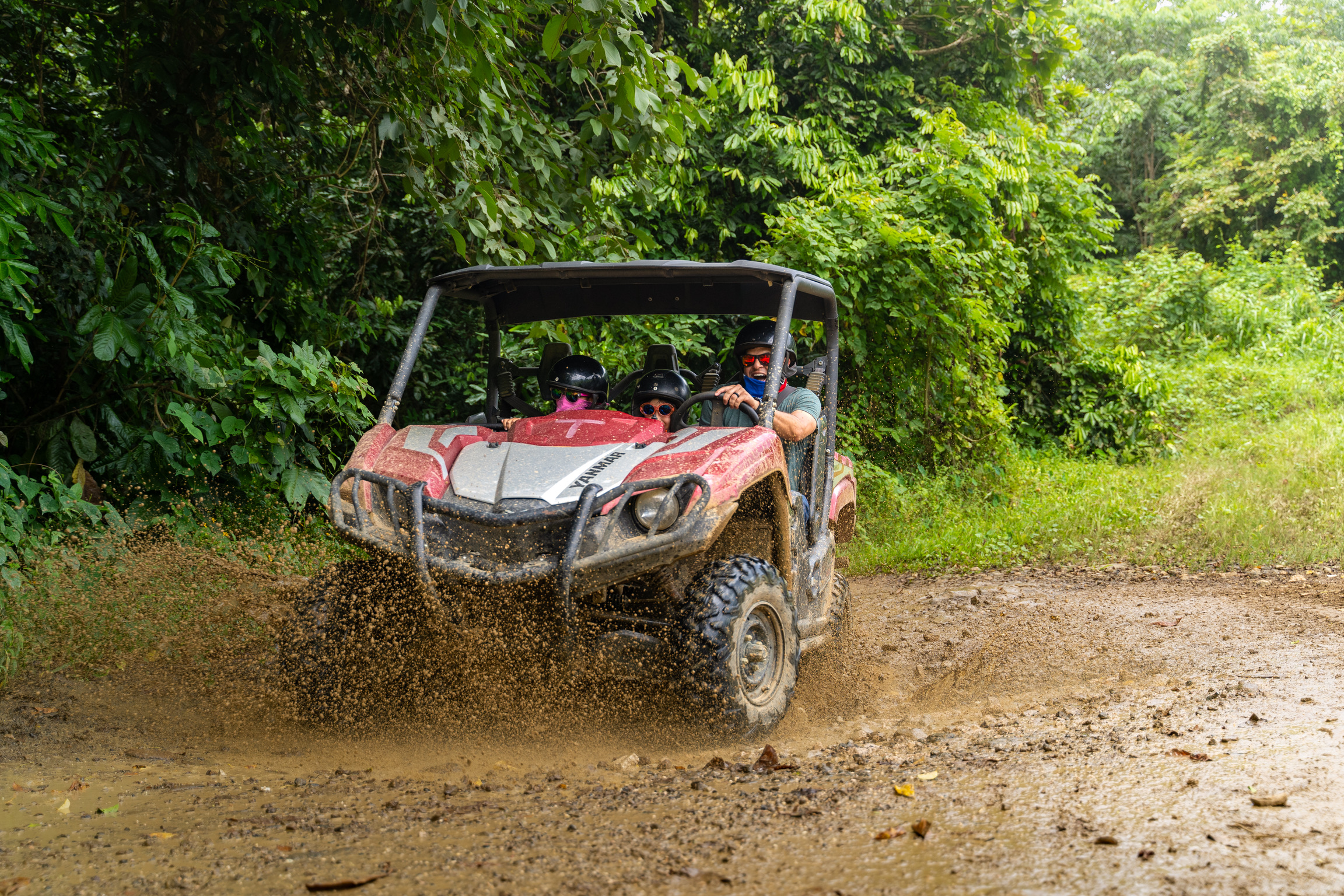 Un quad rojo chapoteando por un camino embarrado en una zona boscosa.