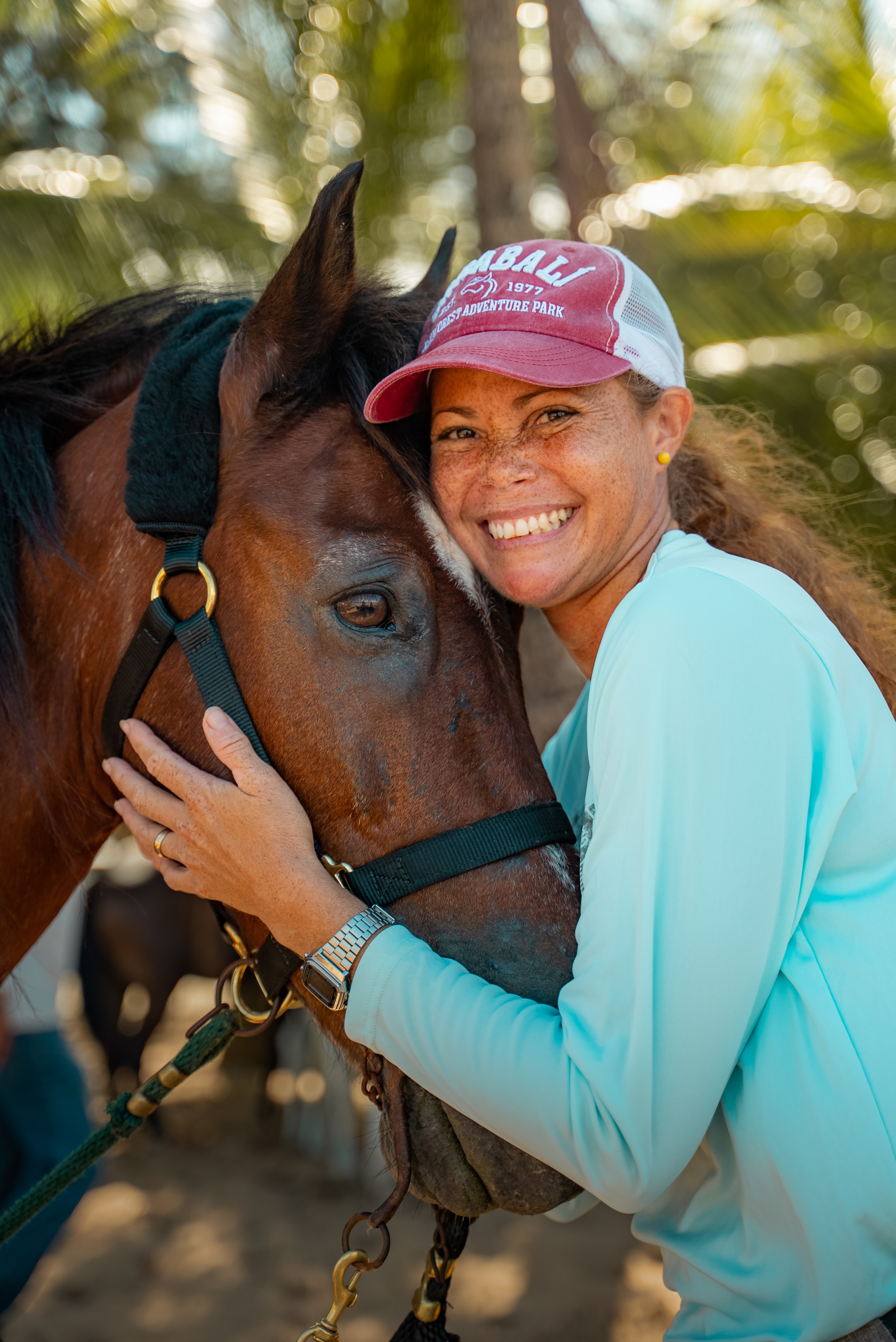 Smiling person in a cap embraces a horse outdoors.