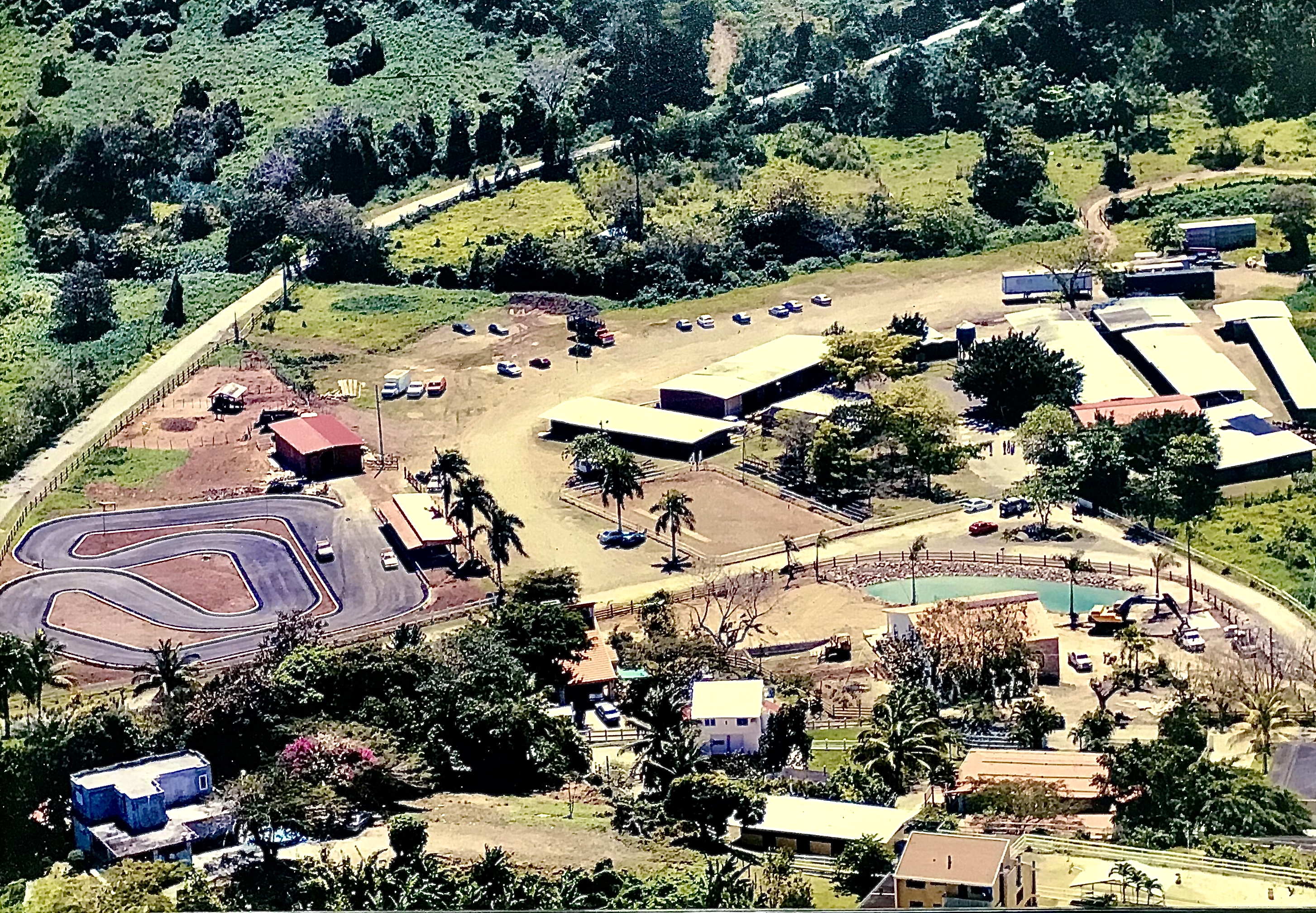 Aerial view of a rural area with buildings, a racing track, and trees.