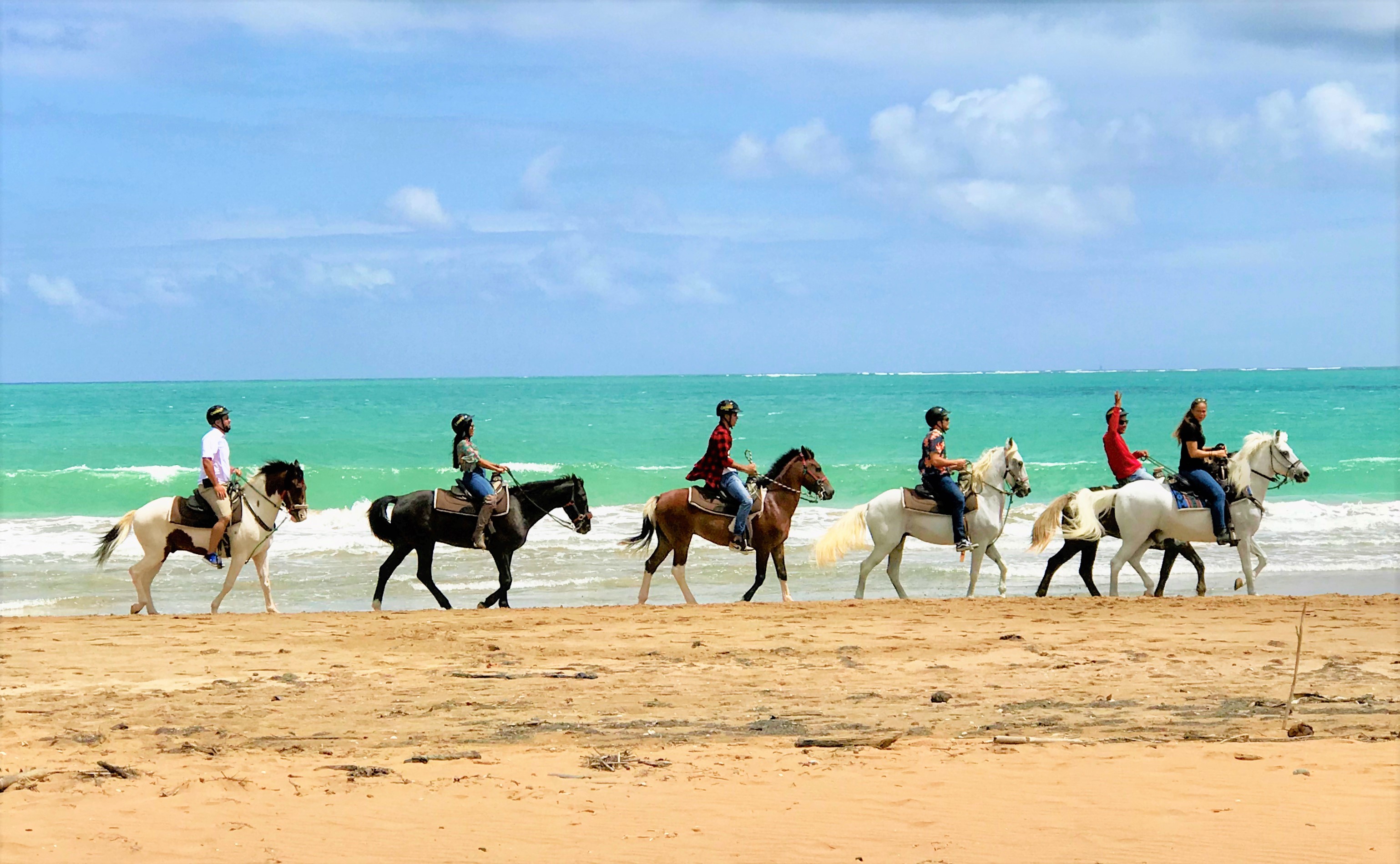 Grupo de personas montando a caballo en una playa junto al océano.