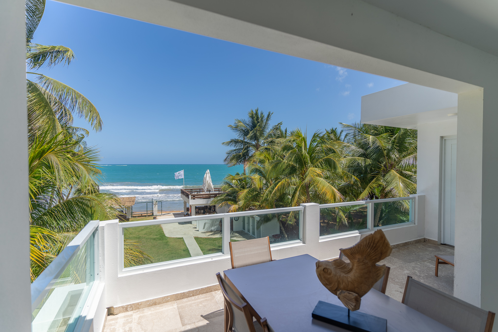 Ocean view from a balcony with palm trees and blue sky.
