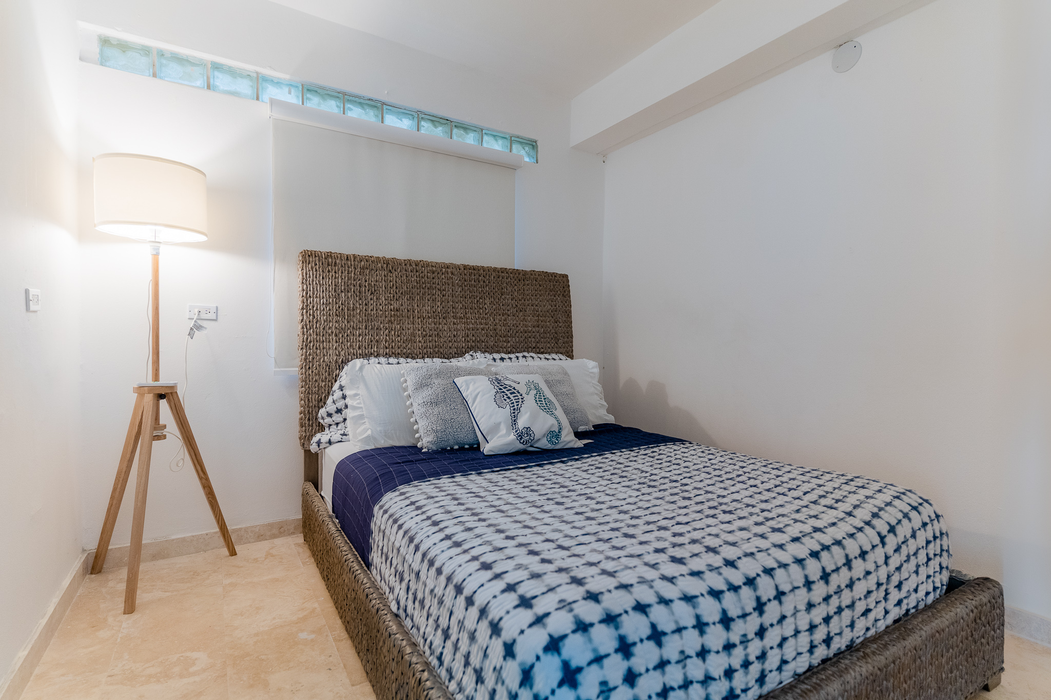 Cozy bedroom with a woven bed, plaid bedding, and a floor lamp in the corner.