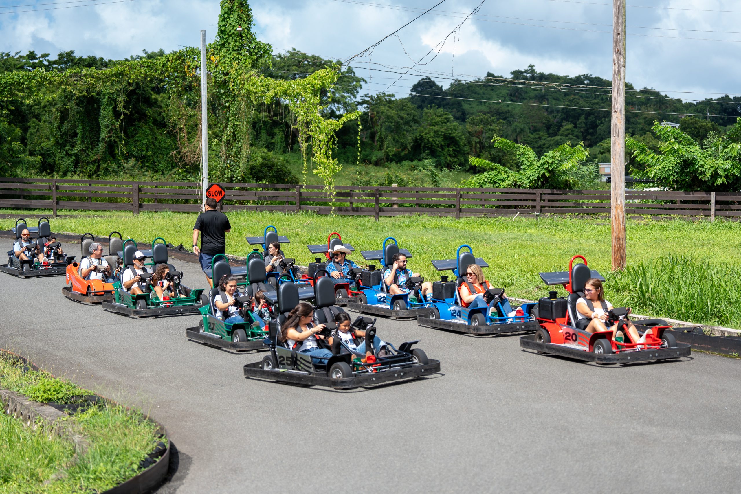 People driving go-karts on an outdoor track near lush greenery.