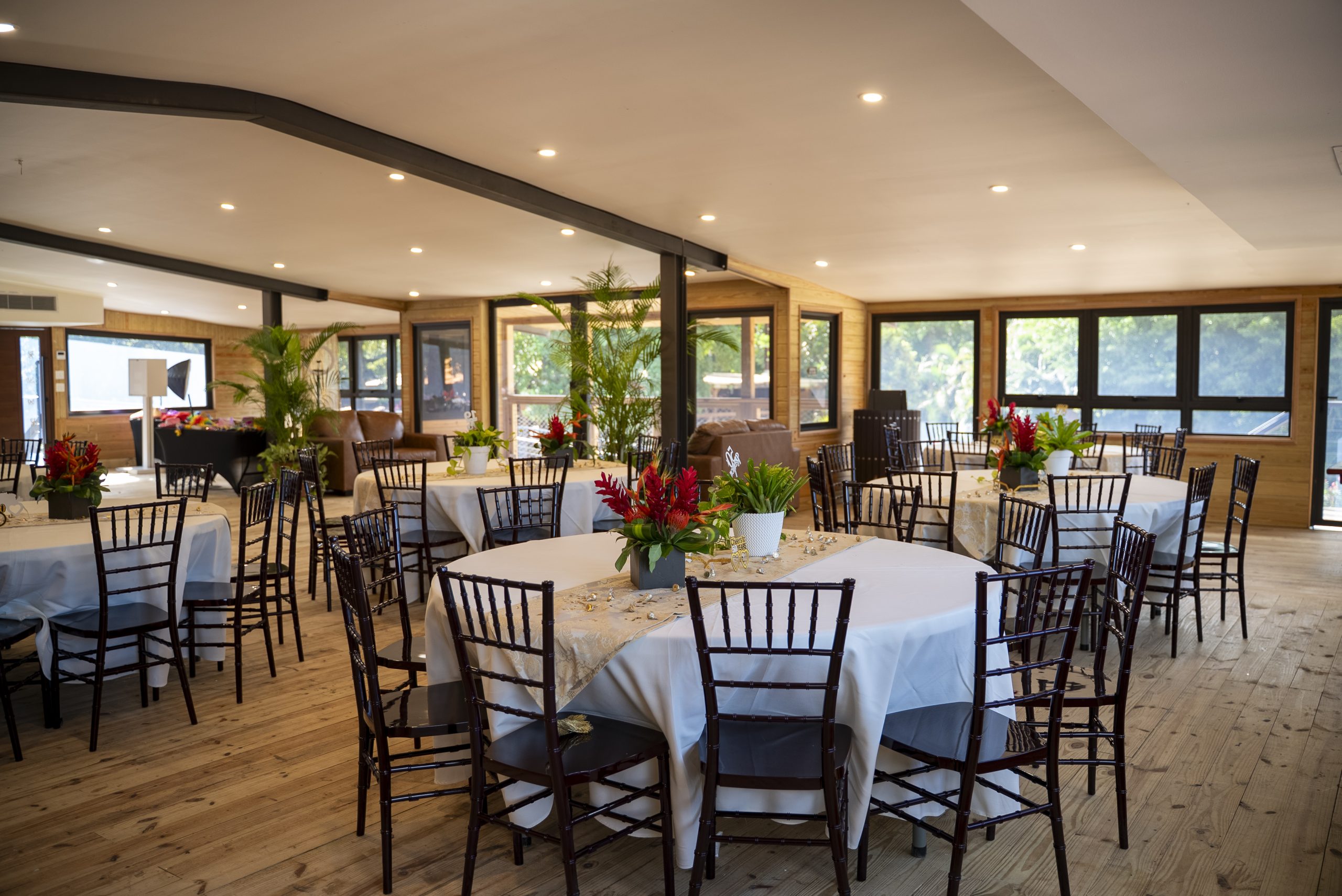 Indoor venue with round tables, white cloths, and floral centerpieces, surrounded by dark chairs.