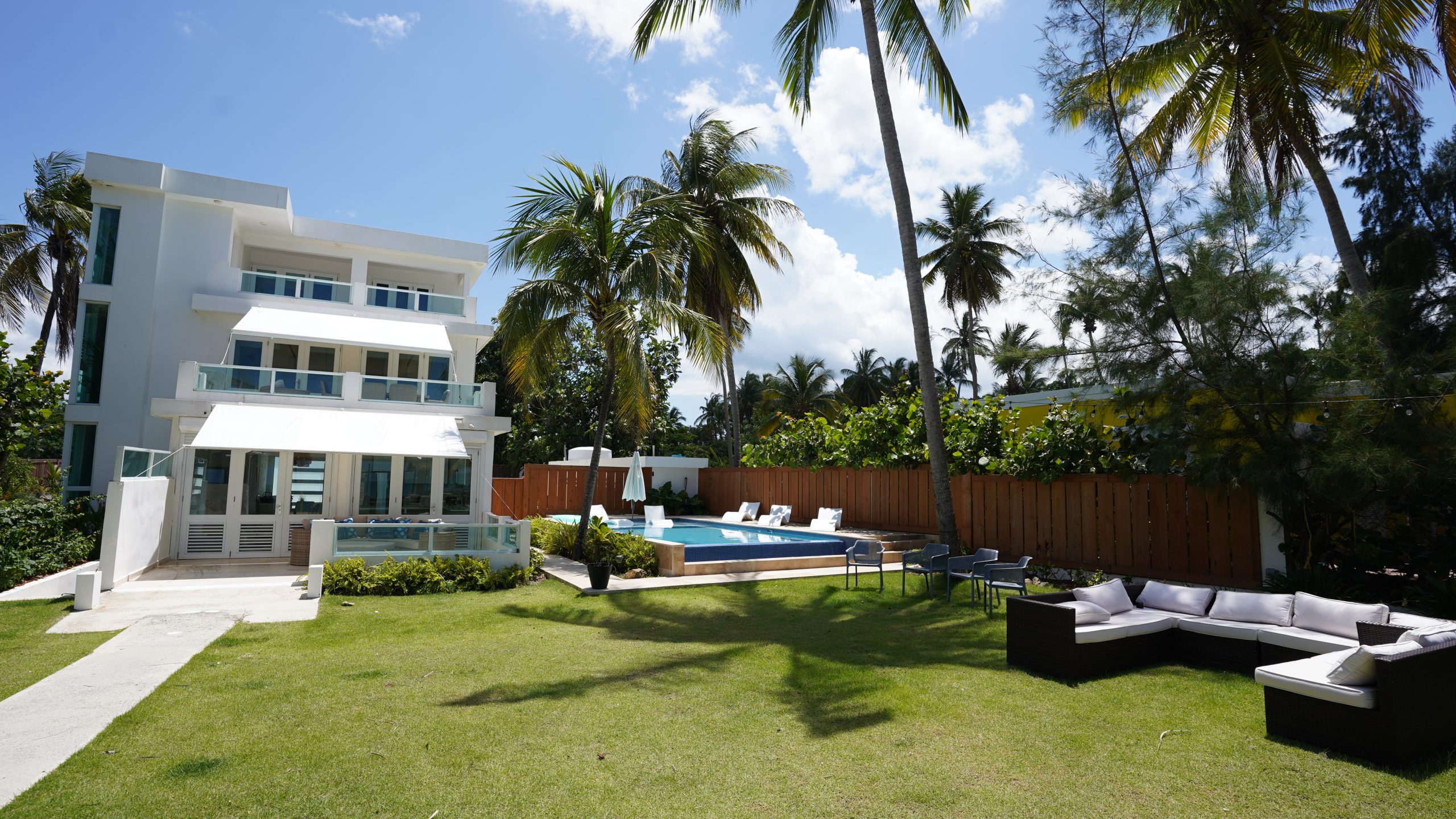 Modern white house with palm trees, pool, and outdoor seating under a clear sky.