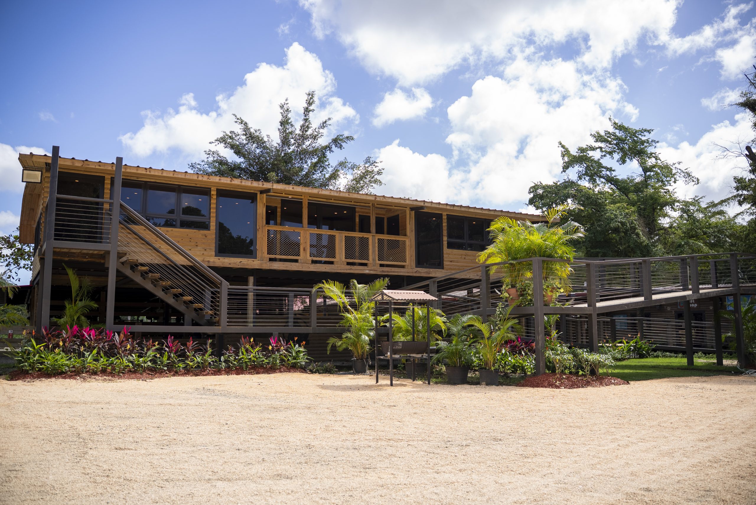 Modern elevated wooden building with stairs and landscaping under a blue sky.